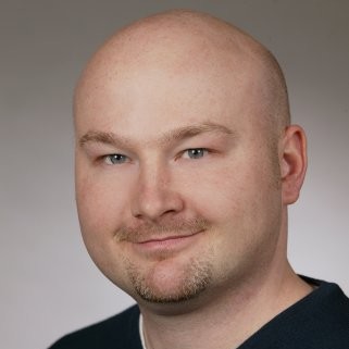 Dave Wascha Head Shot.  Dave smiling in a black tshirt against a neutral background